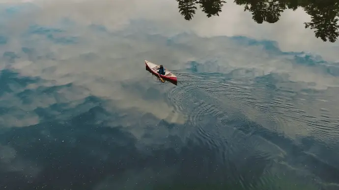 aerial shot from an ottawa documentary, a woman paddles across a lake and create ripples through the reflected clouds