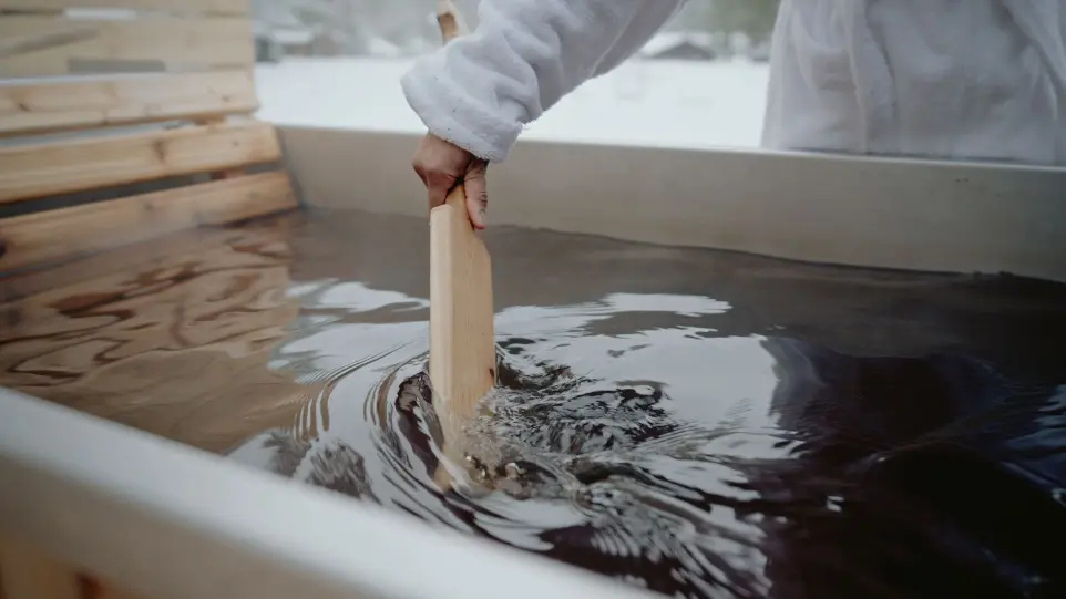 a woman in a robe swills the water of a woodfired hot tub at Anyupaya restort in Ontario