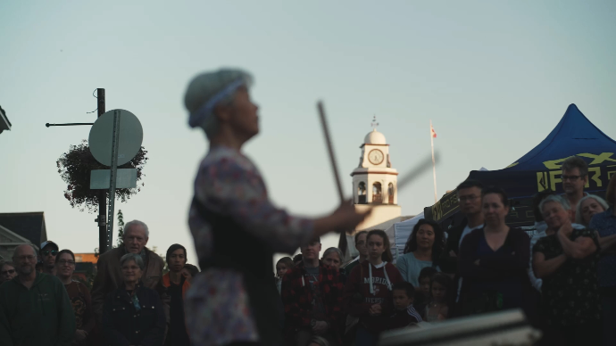 production still  from a video for Perth Ontario, a Japanese woman bangs a drum in front of Perth's town hall