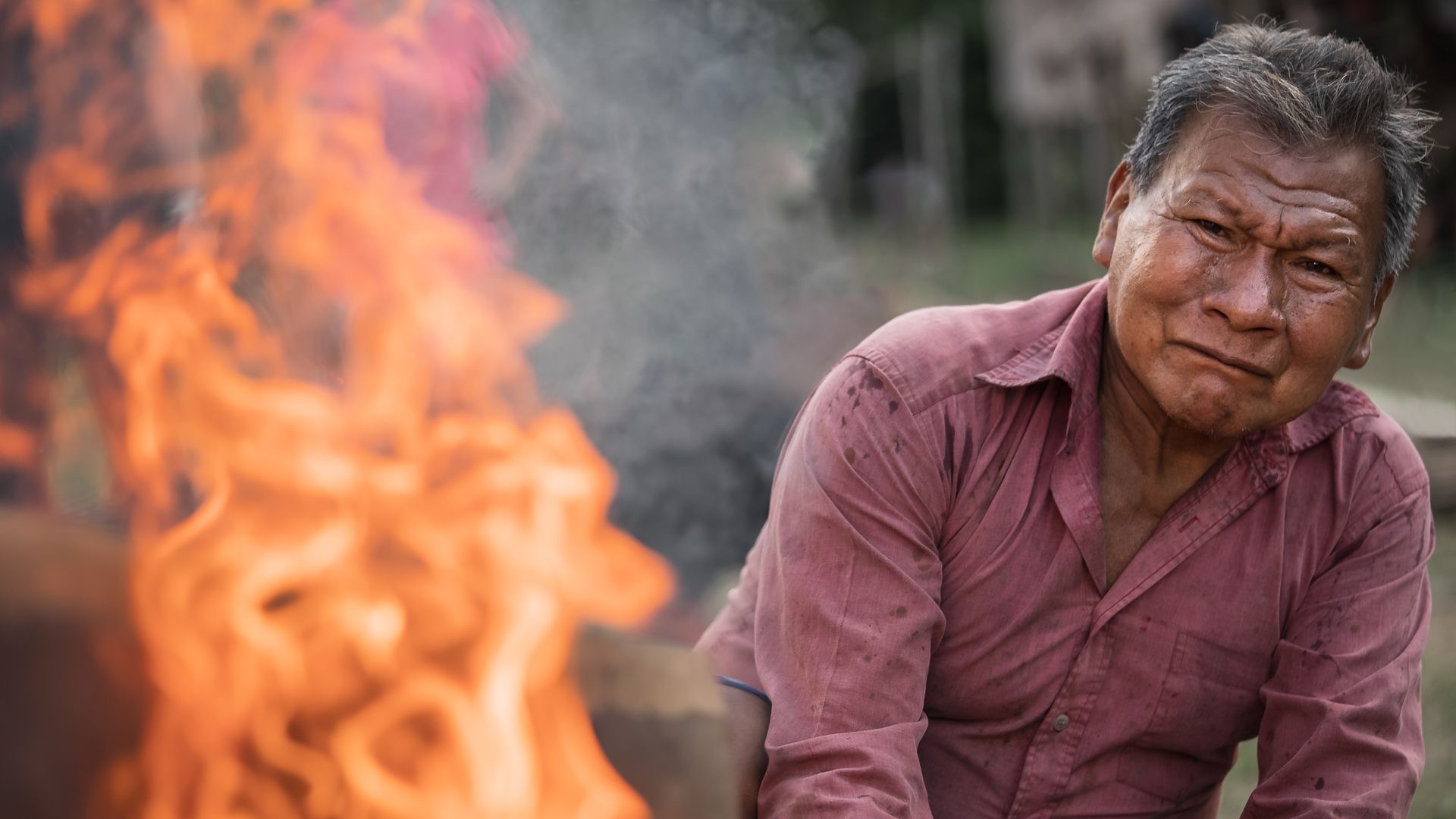 a maijuna man looks at a fire with a pained expression on his face, taken by Ben Hemmings