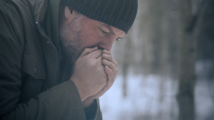 cinematic film still of a man blowing into his hands to keep them warm in the winter