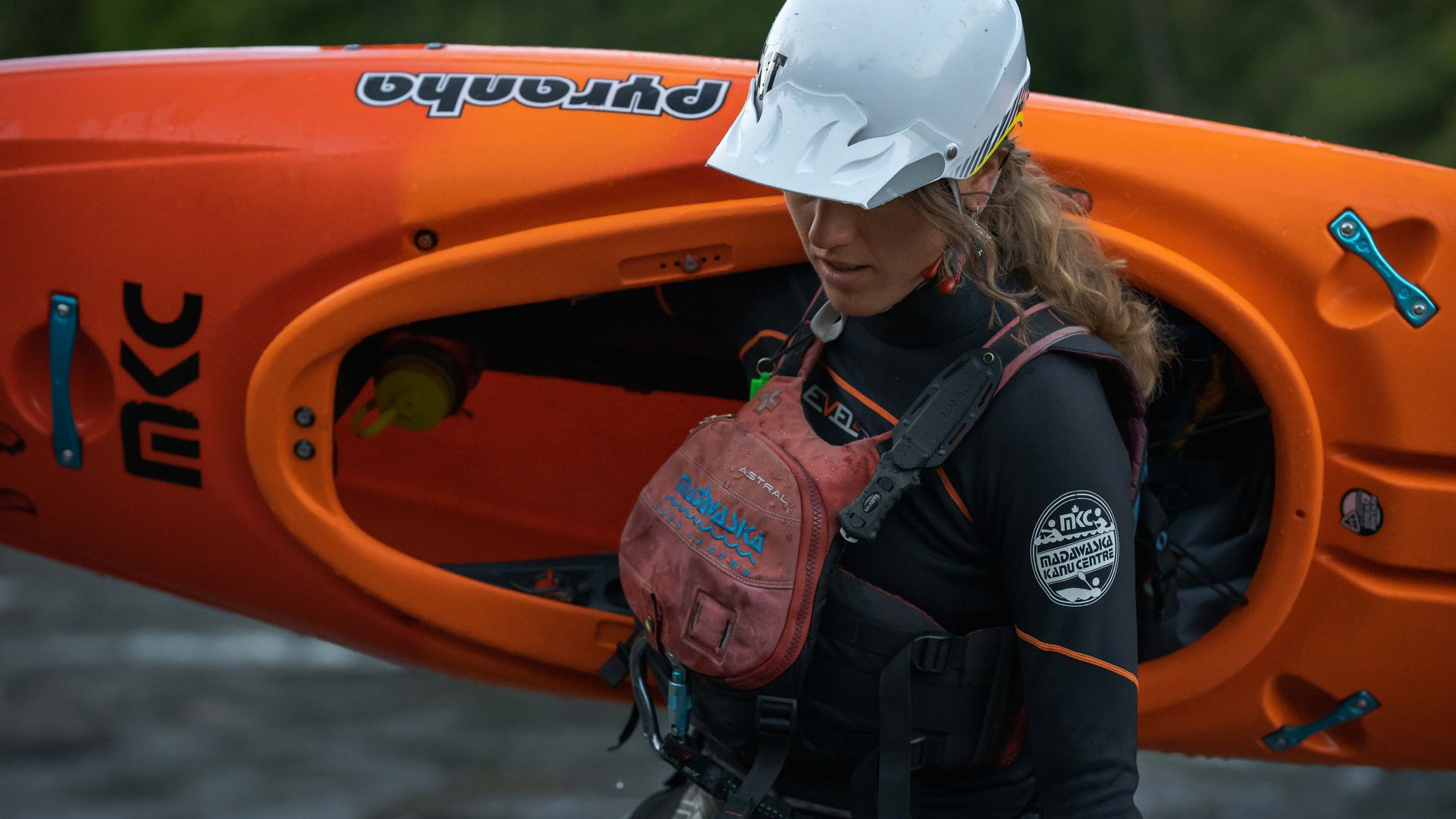 a young woman, Stefi van Wijk, carrying an orange kayak at madawaska Kanu centre in Ontario, a production still from mainspring agency's connections series